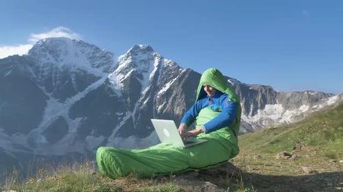 Um indivíduo embalado em um saco de dormir funciona em um laptop contra o pano de fundo do Majestic