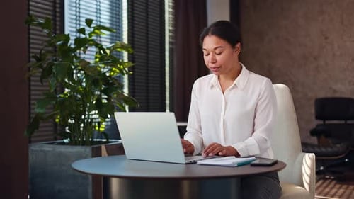 Positive Multiracial Woman Sitting at Office Table and Typing on Portable Laptop