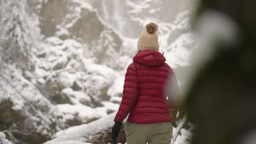 Young Woman Climb up On Rocks And Admire The Snowy And Frozen Cascade du Nant d'Ant Waterfall During