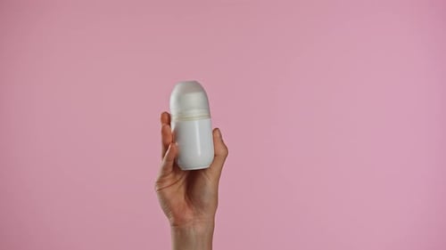 Hand Holding White Deodorant Against Pink Background
