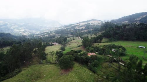Aerial pan shot of a hill filled with greenery all over and hills at background on a foggy day.