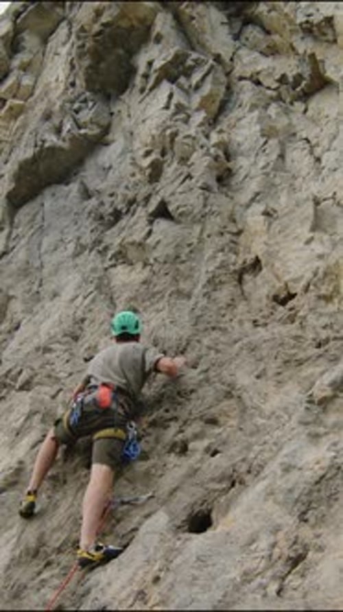 Man Climbing Rock Face while Female Partner Holding Rope