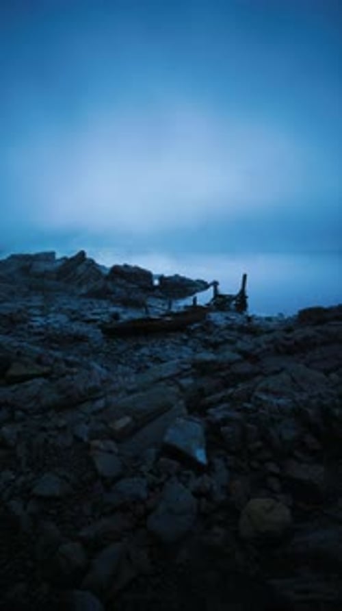 Calm Shoreline at Dusk with Rocks and Driftwood Near the Water