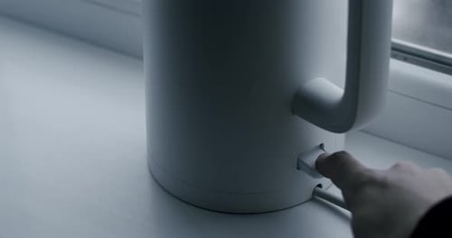 Finger Presses Button on White Electric Kettle