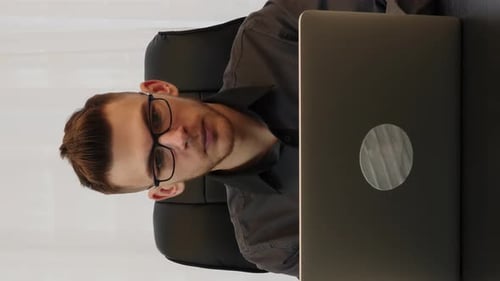 Man in glasses working on laptop computer sitting at workplace. Vertical video