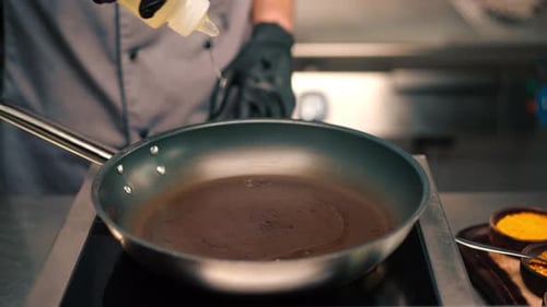 chef in a professional kitchen in a restaurant pouring oil into a pan before cooking close-up