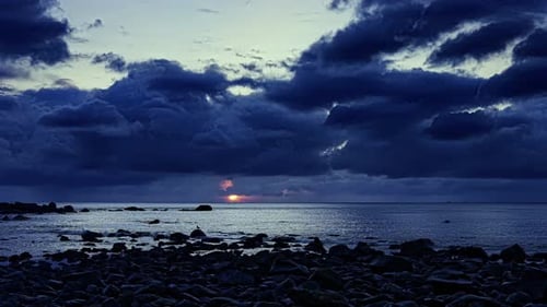 Last moments of the day. Glimpses of the sunset behind heavy dark storm clouds over the wide rocky c