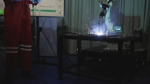 Blue collar workers at workshop with welding robot arm for automotive industry.