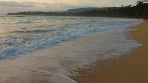 Waves lapping the shore at sunset with a golden glow on the sand and water of the pacific ocean oahu