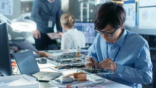 Electronics Engineers Works with Motherboard. Senior Engineer Holds Tablet Computer and Talks with