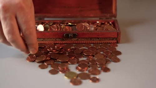 Hand Puts Coins in a Wooden Chest