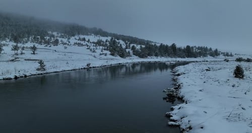 An Aerial View of a Frozen River Flowing Through Snowcovered Forests on a Cloudy Sunset Sky