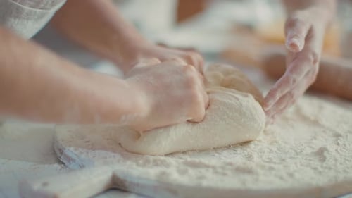 Woman hands helping daughter knead dough with flour in kitchen slow motion
