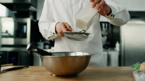 The male chef is sifting flour to the cooking bowl in a professional kitchen cooking in a restaurant