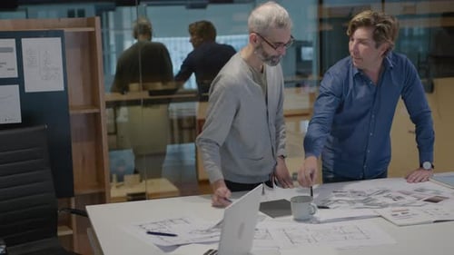 Senior Architect Discussing Floor Plan with Male Coworker in Office