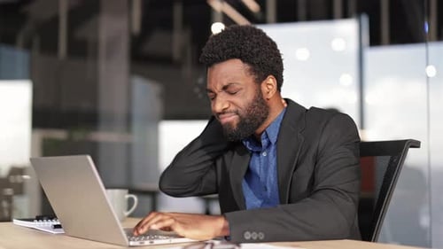 Tired Businessman Suffering From Neck Pain While Working on Laptop in Office
