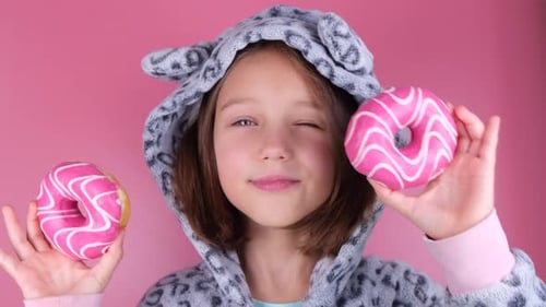 Girl in Kigurumi or Pajamas with Donuts in Place of the Eyes on a Pink Background