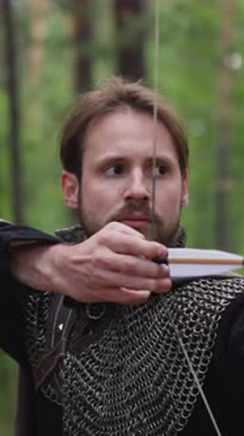 Concentrated Bearded Archer Shoots Bow in Green Wood Closeup