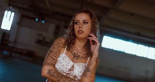 Tattooed woman looks into the camera while a fire breaks out behind her close up