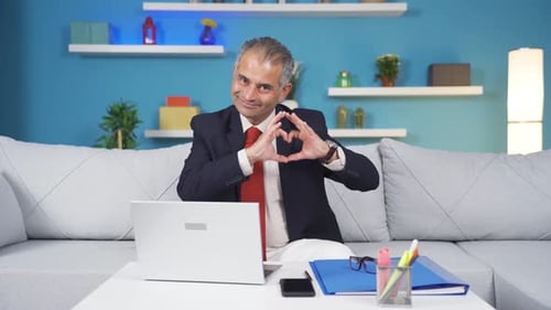 Home office worker man makes heart symbol looking at camera.