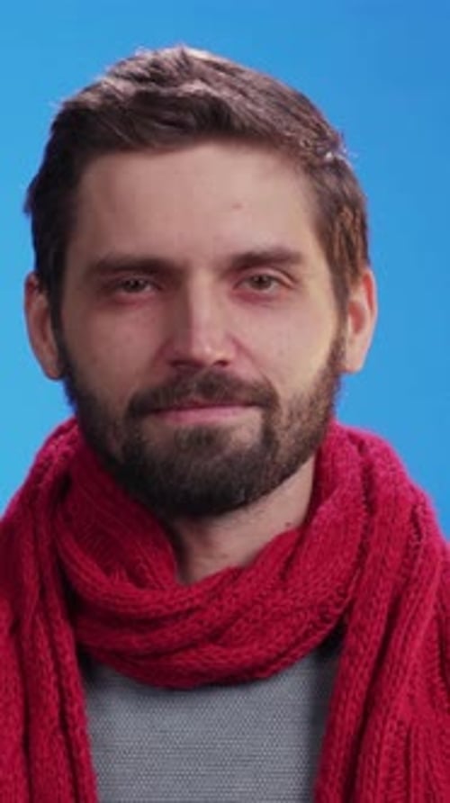 Man Removes Red Scarf in Front of Blue Background