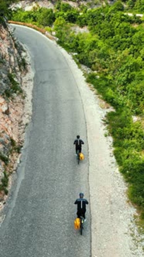 Aerial, drone view of people with yellow backpacks biking on the road in Bosnia and Herzegovina. Ver