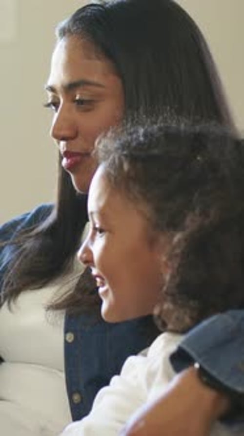 Vertical video: Watching offscreen, mom and daughter on couch, laughing, gasping, arm around child