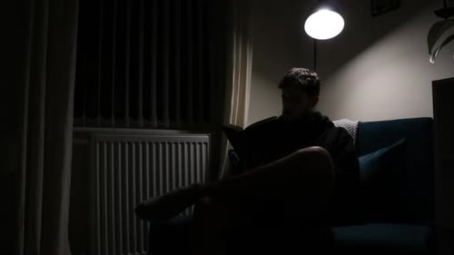 Silhouette shot of man sitting in a corner with a lamp reading his book