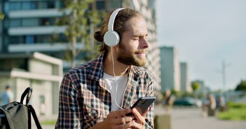 Joyful Young Caucasian Attractive Stylish Man in Headphones Resting at Street and Listening to Music
