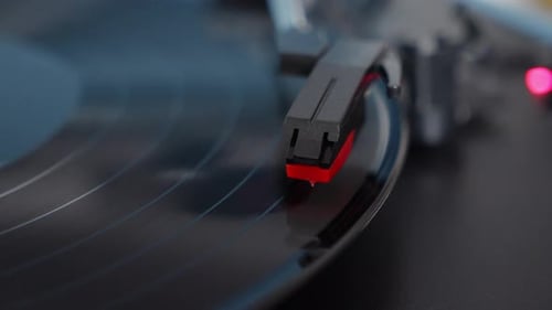 Close-up shot of a vinyl record spinning on a turntable with stylus arm in focus. Vintage analog aud