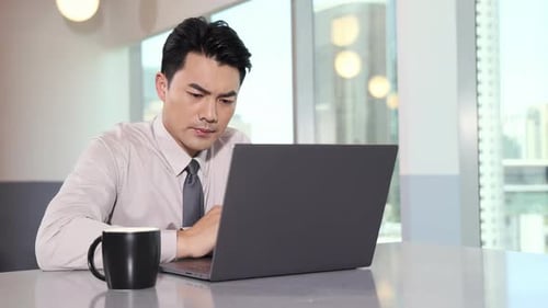 Focused handsome businessman typing on laptop sitting at a workplace in a business office. Business