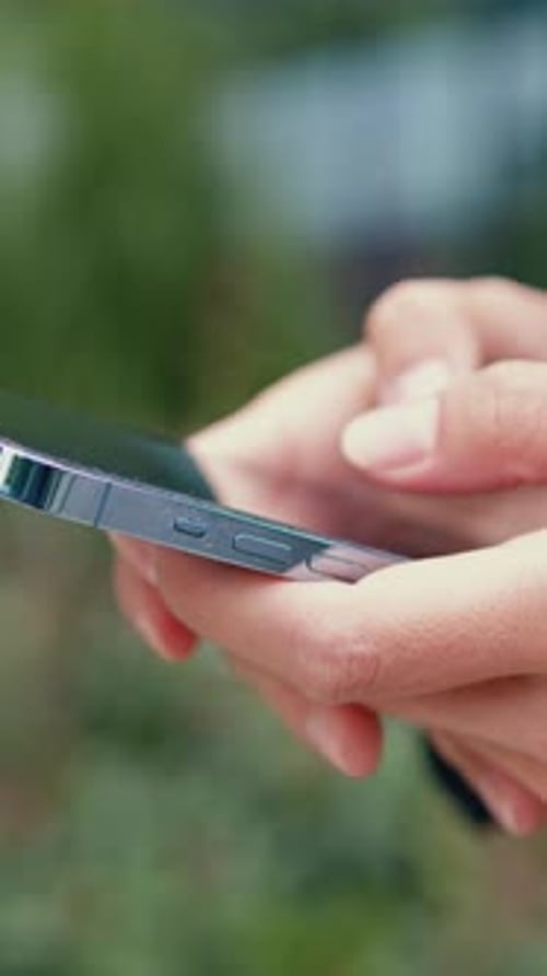 Closeup of a Young Woman Hand Using a Smartphone Outdoors Typing a Message with a Blurred Background