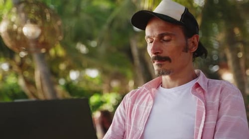 Freelancer arbeitet im Tropical Beach Cafe am Laptop Konzentrierter Mann in Freizeitkleidung inmitten einer Palme