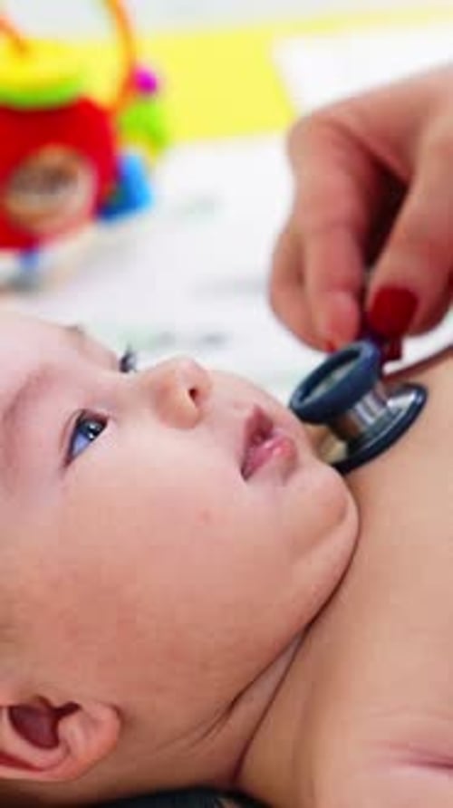 La
main du pédiatre place un stéthoscope sur la poitrine de l'enfant. Le bébé semble intéressé et sourit au médecin.