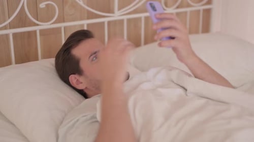 Man Lying in Bed Interacting with Phone