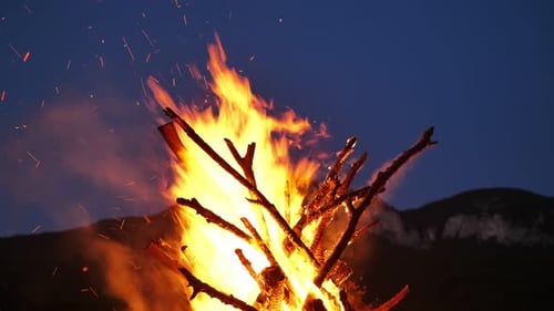 A Huge Bonfire with Sparks on the Background of Mountains and the Night Sky