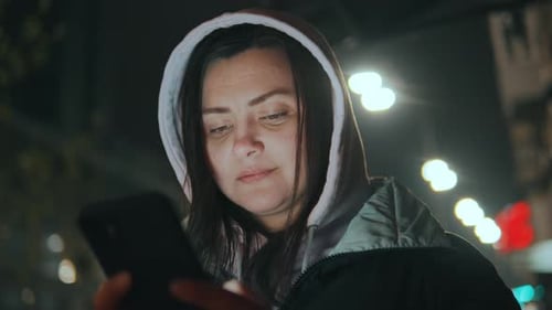 Young Pretty Woman Text Messaging on Her Smart Phone in City Street at Night