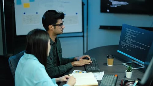 Dois desenvolvedores de software diversos colaboram na codificação em uma mesa de escritório moderna. Trabalho em equipe de tecnologia