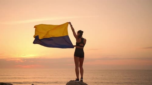 Woman Standing with Ukrainian Flag at Sunset