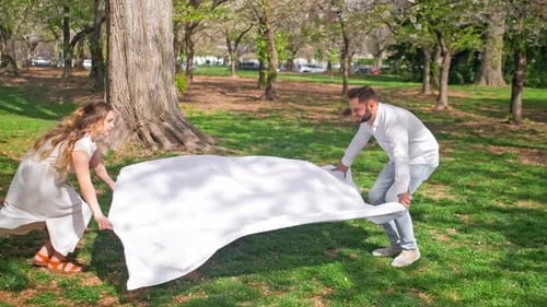 Mom and dad are stretching out a blanket preparing to have a family picnic in a park