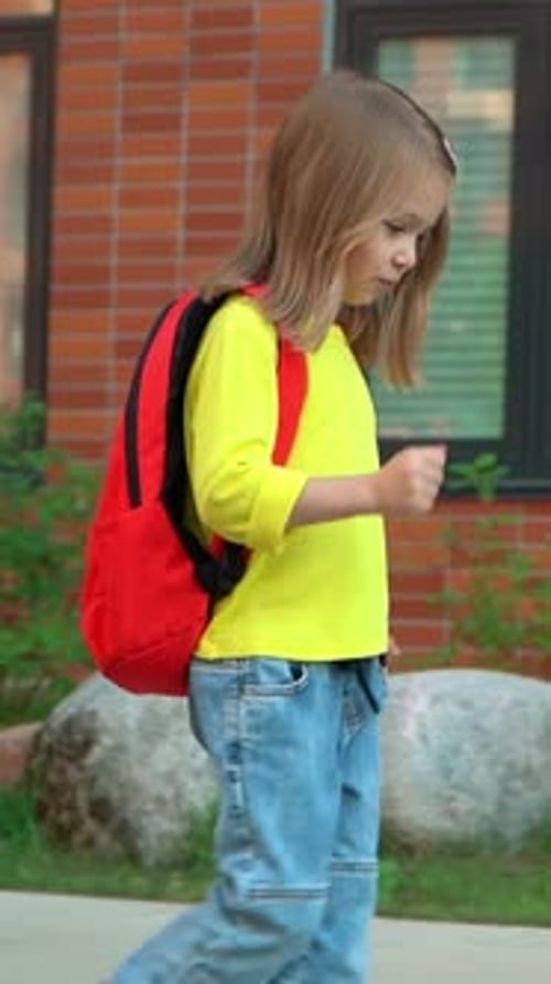 Little Schoolchild Runs and Jumps with School Backpack Outdoors in School Yard