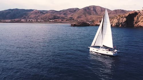 Sailboat sailing by coastline seashore against sunset and mountains. Sail boat in the coast of Spain