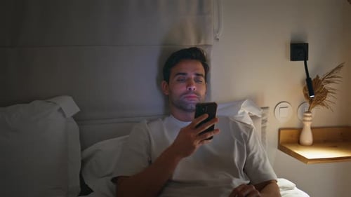 Young Man Using Smartphone in Bed at Night