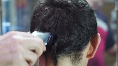 Friseur schneidet einem jungen Mann zu Hause mit Haarschneidemaschine die Haare