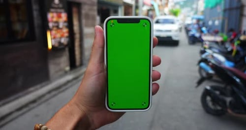 Man's Hand Holding Smartphone with Green Screen Chroma Key Outdoors on Urban City Street Background