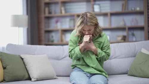 Allergic mature woman coughing because she has seasonal allergies sitting at home. First symptoms
