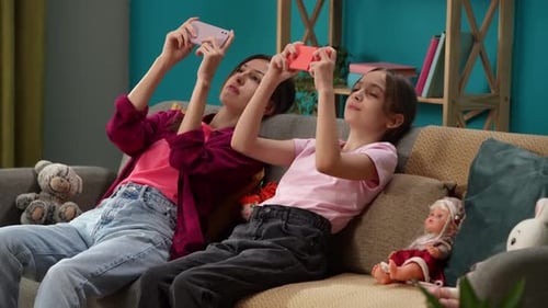 In the Close Up Shot a Mother and Child are Sitting on a Couch in a Room Holding a Phone and