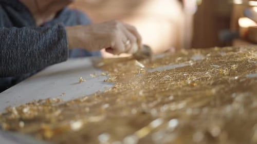 Ein älterer Künstler im Rollstuhl trägt Gold auf das Ölgemälde auf