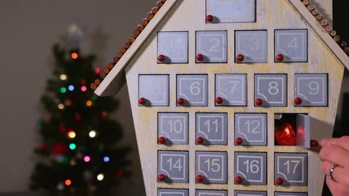 Close up shot of a hand getting candy out of a wooden Advent Calender in front of a Christmas Tree