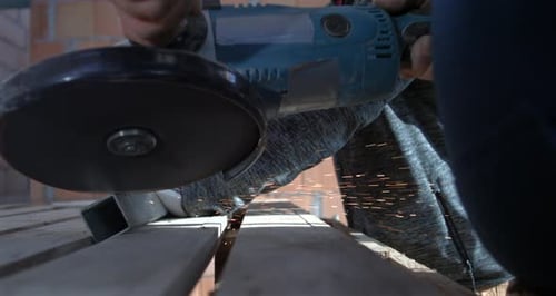 Low-angle view of angle grinder cutting metal, sparks and dust flying, worker’s hand holding tool,